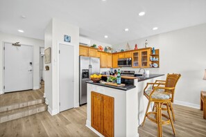 A modern kitchen with wooden cabinets, a stainless steel refrigerator, and a central island with bar stools. - Napili Point | Oceanfront 4 BR, Sleeps 14 | Car Incl. w/ 6+ Nights | NAP ML-3622 by KBM (Lahaina)