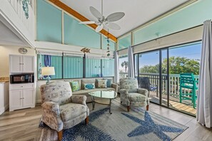 A spacious living room with a large window, a ceiling fan, and a view of the outdoors. - A Wave From It All at Park Place (Cedar Key)