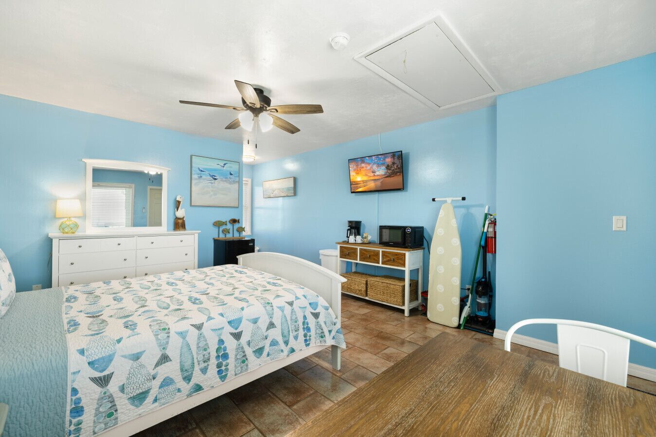 Une chambre à coucher comprenant un lit, une commode, une coiffeuse, un ventilateur de plafond, une télévision et un four à micro-ondes.