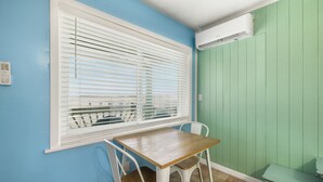 Una habitación con una mesa, sillas, un ventanal con persianas y un equipo de aire acondicionado.