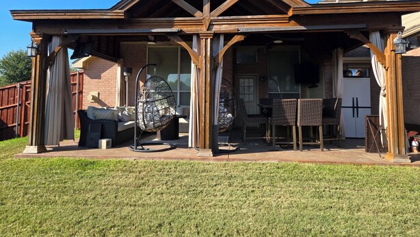 A covered patio area with outdoor furniture, a hanging chair, and a brick house in the background. - Spacious 5-bedroom house in fantastic DeSoto with AC (DeSoto)