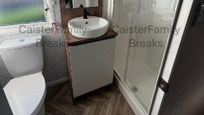 Une salle de bain avec un lavabo blanc, un miroir, des toilettes et un espace douche.