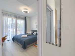 Ein Schlafzimmer mit einem Bett, einem großen Spiegel und Blick ins Freie durch das Fenster.