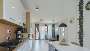 A modern kitchen with a coffee machine, a dining area with a table and chairs, and a living space with a sofa and curtains. - House Bronzin by Interhome (Rovinj/Kanfanar)