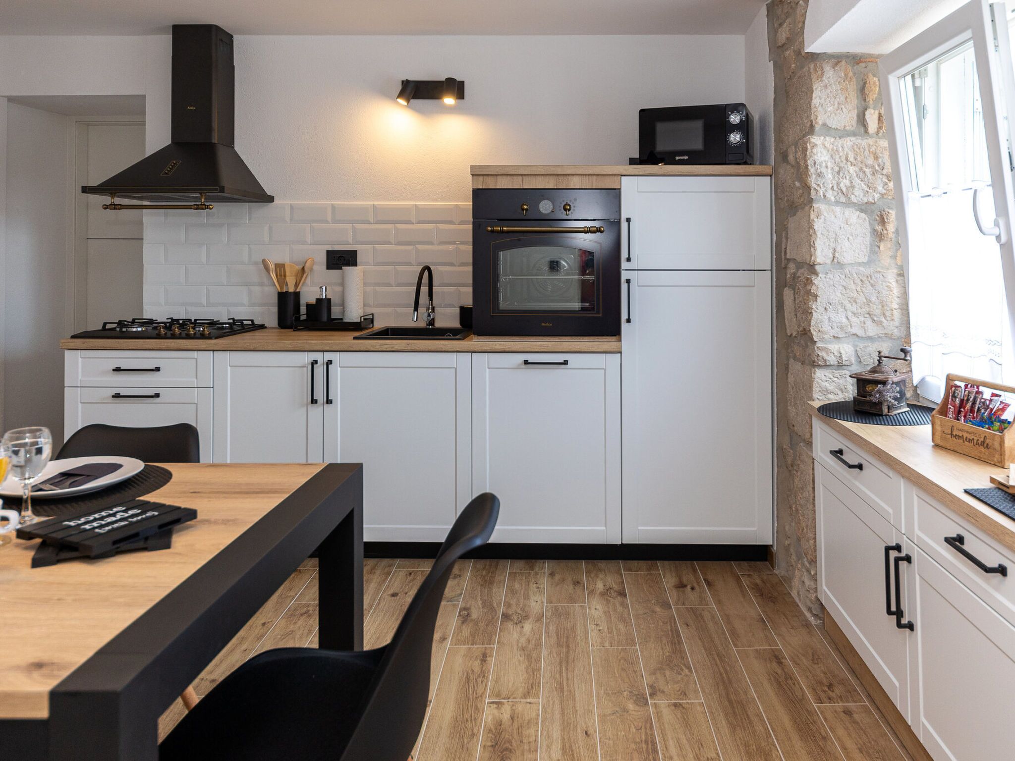 A compact kitchen with white cabinetry, a black stove, a built-in oven, and a microwave on the countertop.