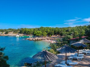 Uma praia costeira com águas azuis cristalinas, guarda-sóis e espreguiçadeiras.