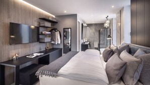 Un dormitorio moderno con cama, mesitas de noche, televisor, vestidor y baño con ducha.