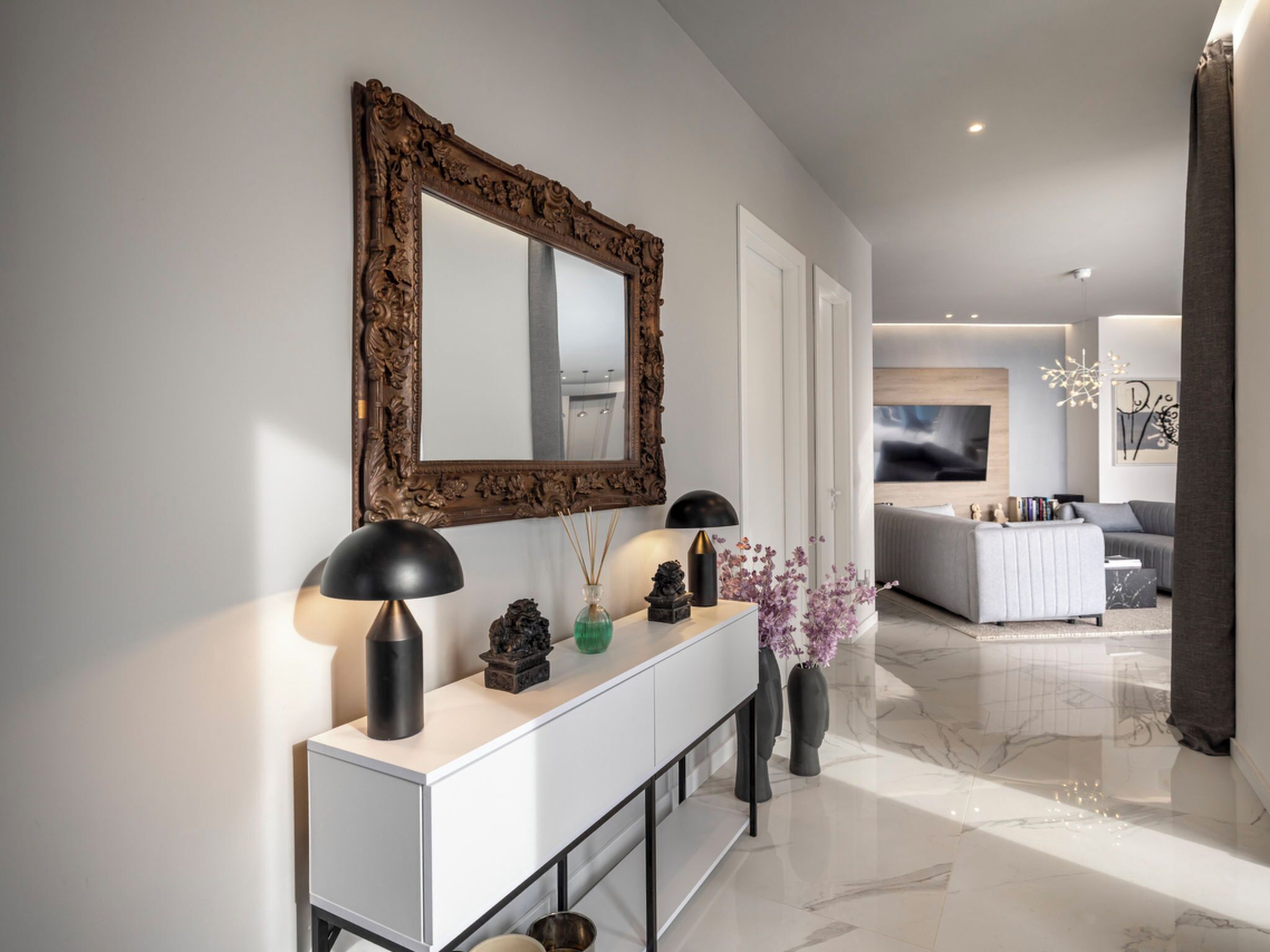 A modern living room with a white console table, a large ornate mirror, and a sofa.