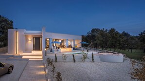 Una casa moderna con piscina, mobiliario exterior y una entrada bien iluminada.