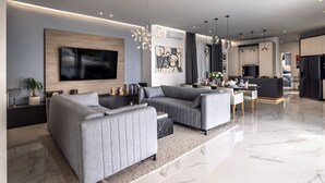 Una sala de estar moderna con un televisor de pantalla plana grande, sofás grises y un comedor con una cocina al fondo.