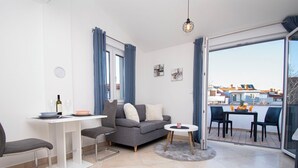 Ein modernes Wohnzimmer mit einer Couch, einem Esstisch und einem Balkon mit Sitzgelegenheiten.