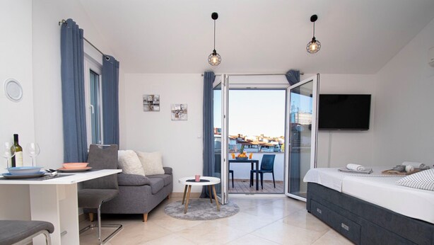 Eine moderne Wohnung mit Essbereich, einer Couch, einem Bett, einem Fernseher und einem Balkon mit Blick auf die Stadt.