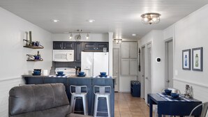 Una cocina moderna con armarios blancos, una isla central con taburetes, un refrigerador y un microondas.