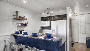 Una cocina moderna con una isla central, taburetes de bar, microondas, refrigerador y estantes empotrados.
