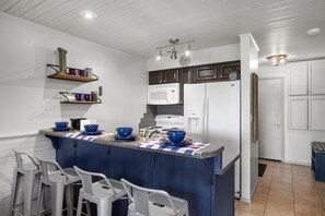 Eine moderne Küche mit einer zentralen Kochinsel, Barhocker, einer Mikrowelle, einem Kühlschrank und eingebauten Regalen.