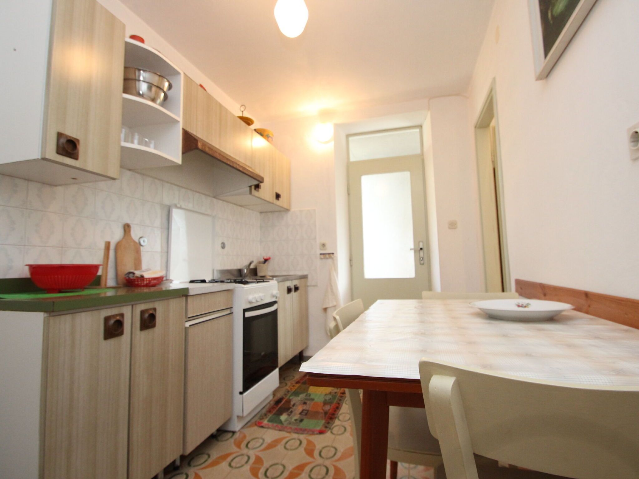 Una cucina compatta con fornelli, forno e mobili in legno. C'è un tavolo da pranzo con sedie e un tappeto decorato.