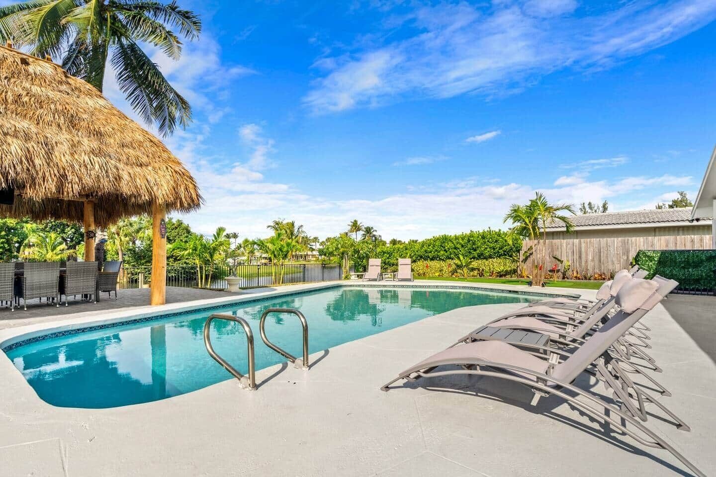 A swimming pool with lounge chairs, a thatched roof structure, and palm trees.