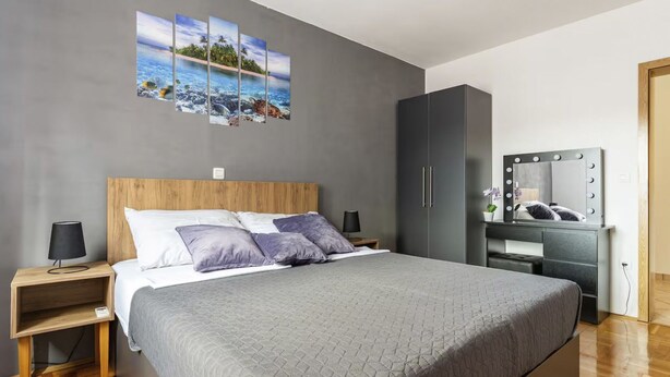 Ein modernes Schlafzimmer mit einem großen Bett, Nachttischen, einem Kleiderschrank und einem an der Wand befestigten Spiegel.