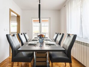 A dining room with a long table, black chairs, a central light fixture, and a window with blinds. - Apartment DP by Interhome (Bokordici)