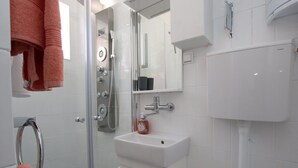 Un bany amb dutxa trencadissa, un lavabo blanc i un mirall a sobre.