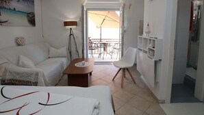 Habitació d'hotel amb llit, sofà, taula petita, cadira, balcó amb una ombrel·la i vista al mar.