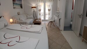 Habitació d'hotel amb llit, cadira, taula petita, làmpada, quadre i vista a l'exterior.