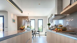 A modern kitchen with a central island, a dining area with a table and chairs, and a view through large windows. - Villa Grande by Interhome (Poreč/Tar)
