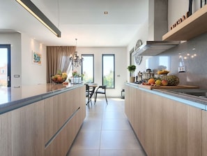 Une cuisine moderne dotée d’un îlot central, d’un coin repas avec une table et des chaises, et offrant une vue dégagée grâce à de grandes fenêtres.