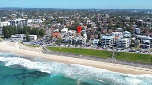 A coastal cityscape with a beach, buildings, and a red location marker. - Popular North Cronulla Beach Apartment sleeps up to 5 people (Cronulla)