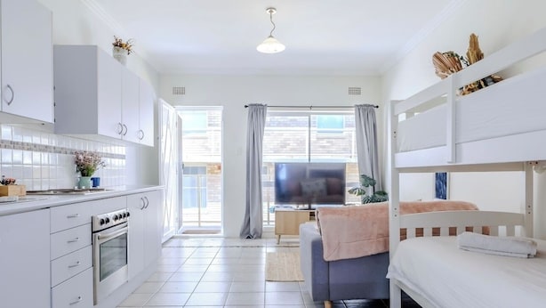 A modern, well-lit room with a kitchenette, a sofa, and a bunk bed. - Popular North Cronulla Beach Apartment sleeps up to 5 people (Cronulla)