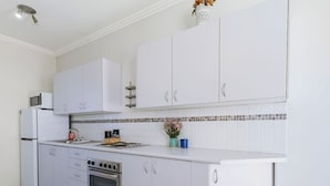 A modern kitchen with white cabinets, a built-in oven, and a microwave. - Popular North Cronulla Beach Apartment sleeps up to 5 people (Cronulla)