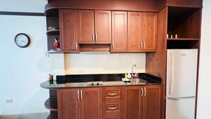 A kitchen with wooden cabinets, a stainless steel countertop, and a white refrigerator. - Japanese Styled Condo in the Heart of Pattaya next to Pattaya Beach. (Pattaya City)