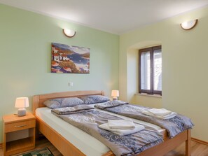 Ein Schlafzimmer mit einem Bett, zwei Nachttischlampen, einem Nachttisch, einem Fenster und einem Bild an der Wand.