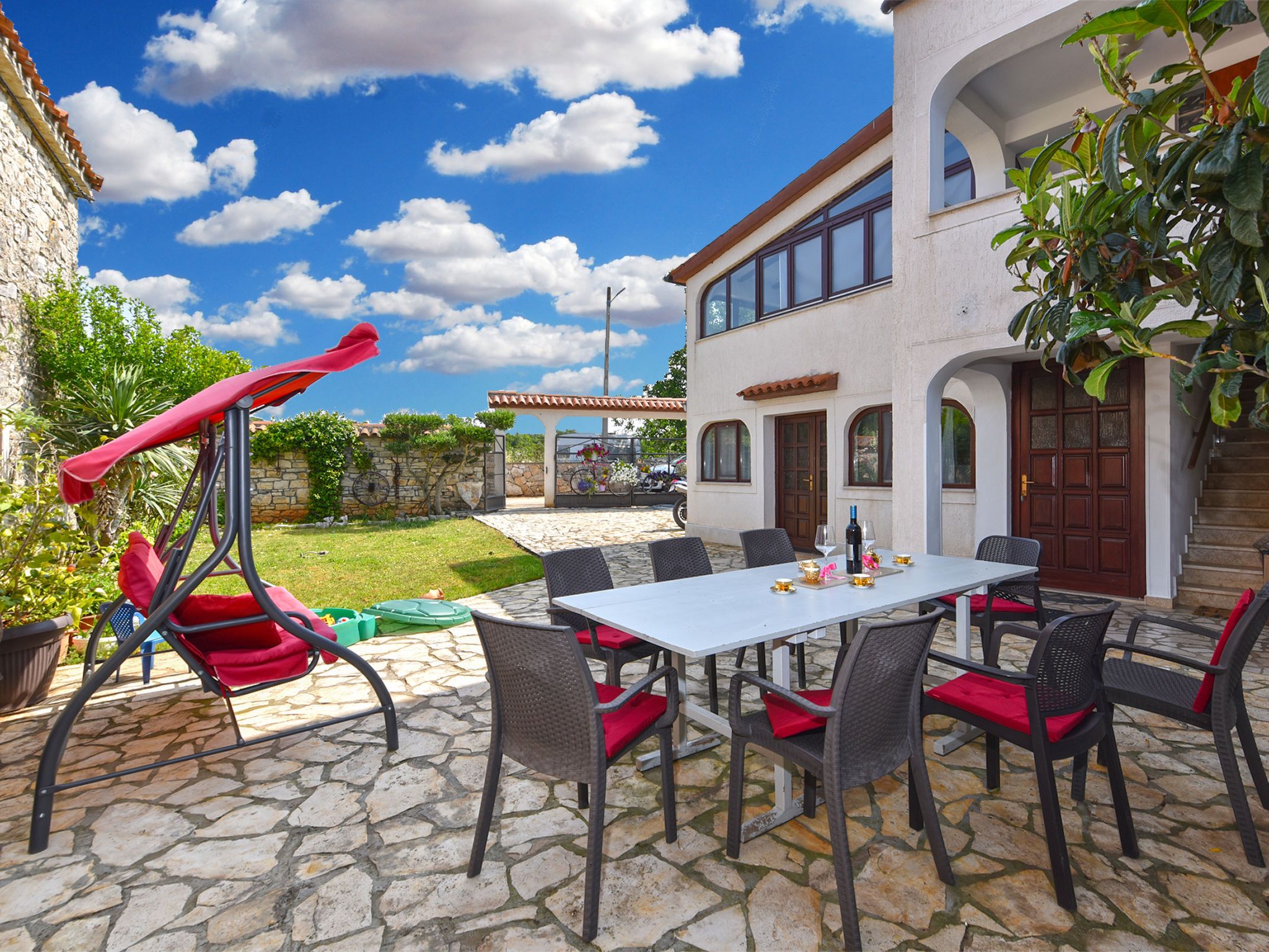 A patio with a stone floor, a white table, and red chairs.