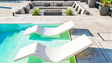 A pool area with two lounge chairs, a seating area with cushions, and potted plants.