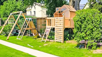 A backyard with a wooden playhouse, a swing set, and a slide.