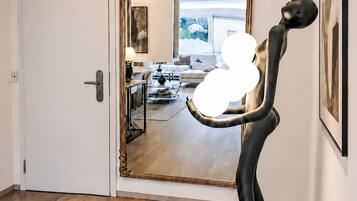Ein Zimmer mit einem großen Spiegel, der einen Wohnbereich reflektiert, einer Tür mit moderner Griffleiste und einem hellen Holzboden.