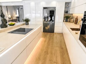 A modern kitchen with white cabinetry, a stainless steel refrigerator, and a wooden floor.