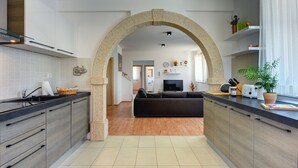 Eine moderne Küche mit einem Steingewölbe, das in einen Wohnbereich führt, Holzböden und einem schwarzen Sofa.