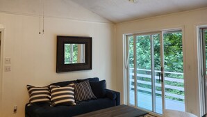 A living room with a ceiling fan, a dark-colored sofa, a wooden coffee table, and a large window with a view of greenery. - The Blue Dove (Shenandoah Farms)