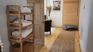 A room with a wooden floor, a rattan storage unit, a black chair, a wooden door, and a framed picture on the wall. - The Blue Dove (Shenandoah Farms)