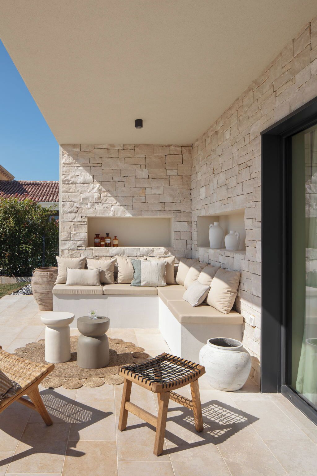 An outdoor seating area with a stone wall, a cushioned bench, and a small table.