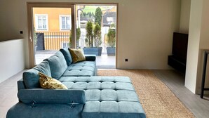A modern living room with a sectional sofa, a flat-screen TV, and a view of a balcony with potted plants. - Z Apartment by Interhome (Schladming)