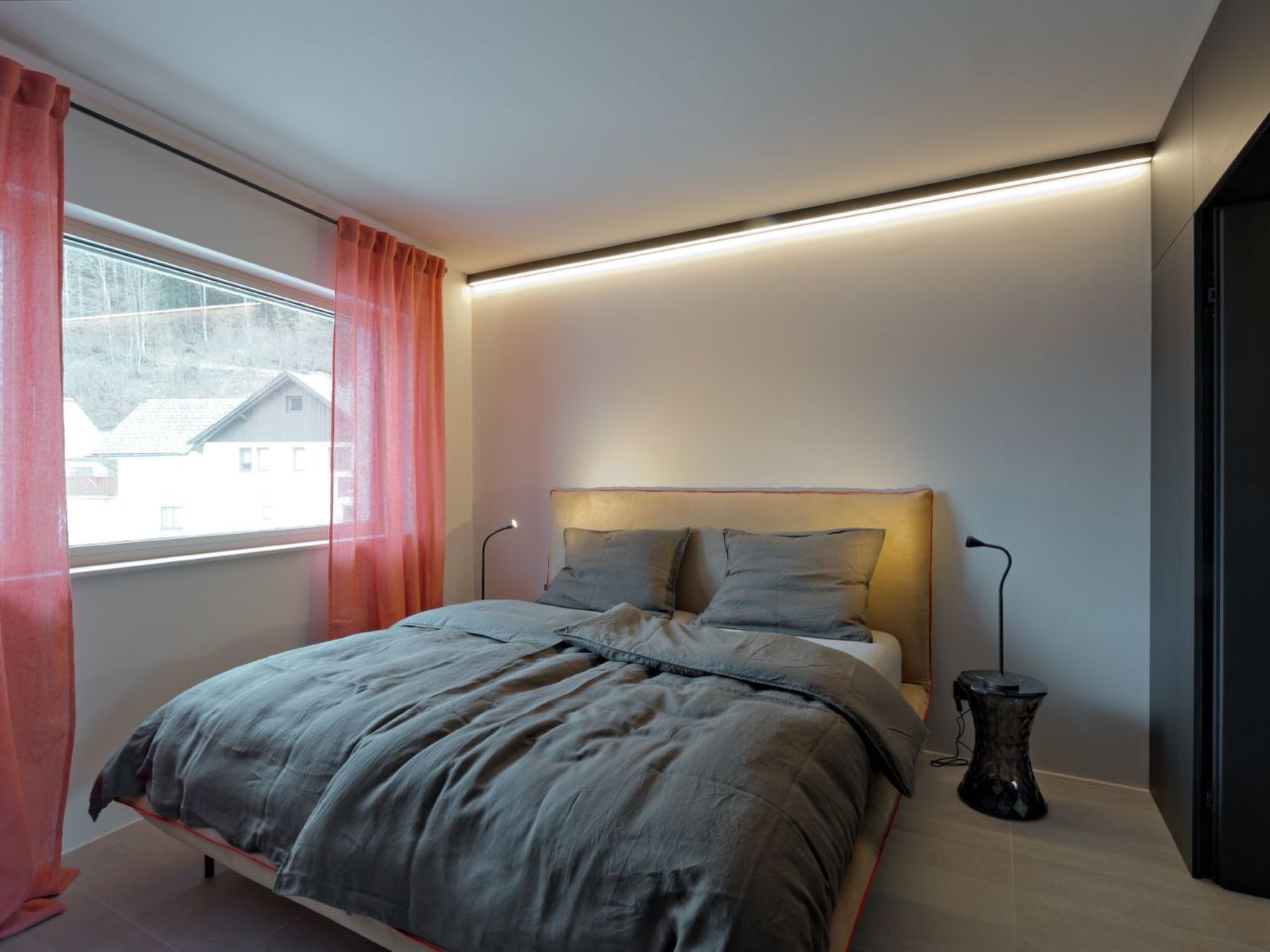 Un dormitorio moderno con una cama, una mesita de noche y un ventanal con cortinas.