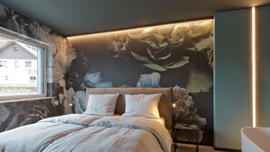 A modern bedroom with a large bed, a nightstand, a wall-mounted lamp, and a bathtub. - Z Apartment by Interhome (Schladming)