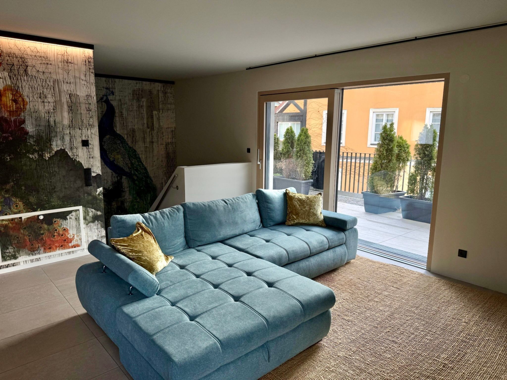 A modern living room with a light blue sectional sofa, a large abstract painting, and a view of the outside balcony.