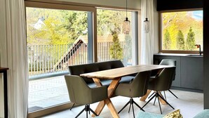A modern dining area with a wooden table and black chairs, large sliding glass doors, and a view of a balcony with a railing. - Z Apartment by Interhome (Schladming)