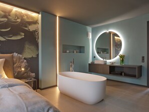 Een moderne badkamer met een vrijstaand bad, een ronde spiegel met verlichting en een minimalistische wastafel.