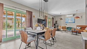 Een moderne woonkamer met een eethoek, grote ramen en uitzicht op buiten.