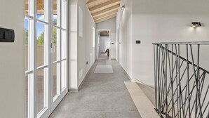 Een modern interieur met een gang die leidt naar een kamer, met een houten plafond, grote ramen en een metalen leuning.
